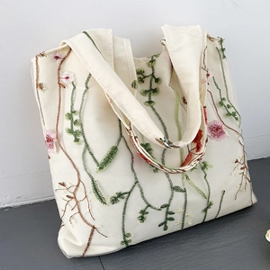Detailed close-up of floral embroidery on off-white canvas tote bag with mesh overlay