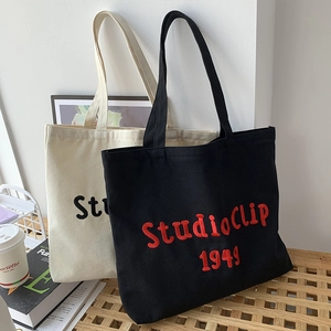 Detail of StudioClip 1949 canvas tote bags in cream and black on a rustic wooden table