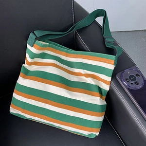 Striped canvas crossbody bag with green orange and white stripes on a leather sofa