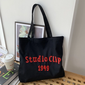 Close-up of red embroidered text on a black canvas tote bag in a minimalist indoor setting