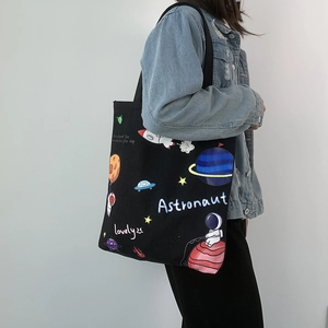 Detail of black canvas tote bag with astronaut space print worn by model on shoulder