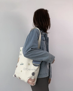 Detail view of white canvas tote bag featuring astronaut planet illustrations and long straps