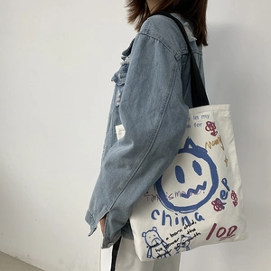 Detail of white canvas tote bag featuring blue bear graffiti and black shoulder straps
