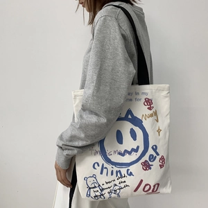 Detail of white canvas tote bag featuring colorful graffiti prints and a shoulder strap