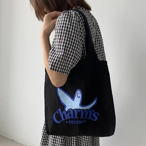 Detail of black canvas tote bag showing blue cartoon print and Charm's STUDIO brand logo