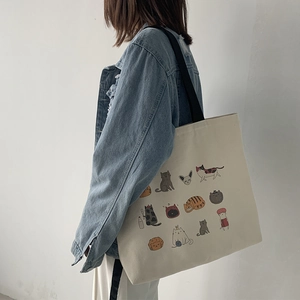 Détail latéral d'un sac cabas en toile blanc cassé orné d'illustrations de chats de dessin