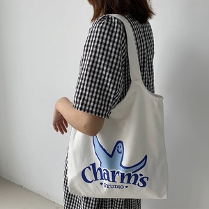 Close-up of white canvas tote bag with blue cartoon print and Charm's STUDIO text detail