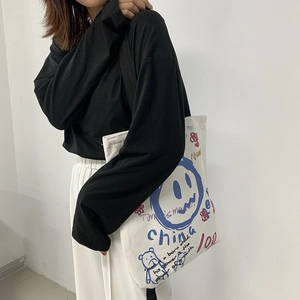 Detail of off-white canvas tote bag featuring artistic graffiti prints and black straps