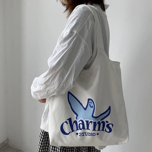 Detail of white canvas tote bag featuring blue smiley face and Charm's STUDIO print