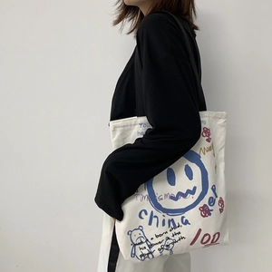Detail of white canvas tote bag featuring blue graffiti smile face and bear illustrations