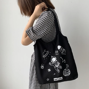 Detail shot of black canvas tote bag with astronaut print worn over a checkered dress