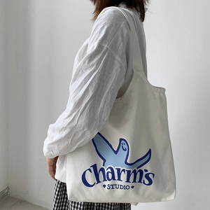 Detail of white canvas tote bag featuring blue Charm's logo and playful graphic