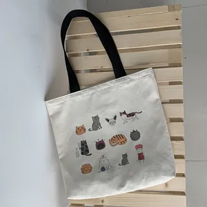 Vue détaillée du sac cabas en toile crème avec divers motifs de chats et des anses noires