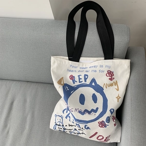 Detail of white canvas tote bag with blue cat graffiti and multicolor text on sofa