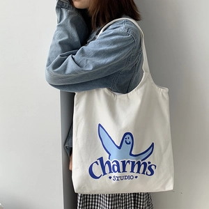 Detailed view of white canvas tote bag featuring a blue cartoon print and fabric texture