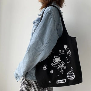 Close-up of black canvas tote bag featuring white astronaut space print on model