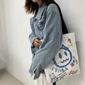 Detail of a large off-white canvas tote bag with blue smiley face and street graffiti prints