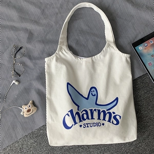 Detail shot of white canvas tote bag with blue cartoon print and Charm's Studio text