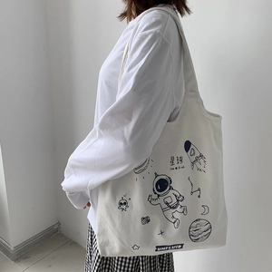 Detail of white canvas tote bag featuring navy blue astronaut and space theme illustrations