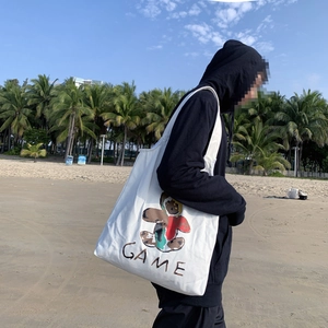 Grand sac fourre-tout blanc en toile avec imprimé ours porté à l'épaule sur une plage d'été