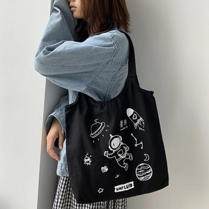Detail of black canvas tote bag featuring white space planet illustrations and shoulder strap