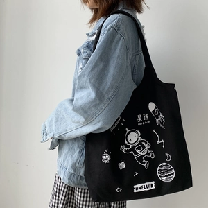 Black canvas tote bag with astronaut graffiti print styled on a model's shoulder
