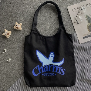 Flat lay of black canvas tote bag with cartoon print, glasses, and earbuds setup