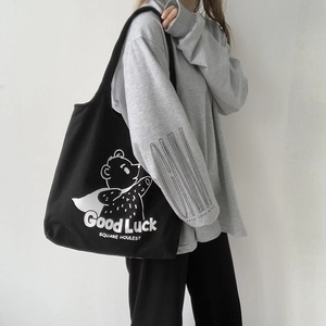 Detail of black canvas tote bag with cartoon bear print and slogan on model's shoulder