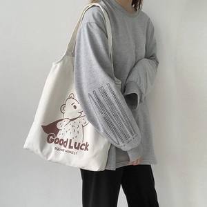 Detail of off-white canvas tote bag featuring brown cartoon bear and lucky text print