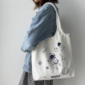 Close-up of white canvas tote bag with blue space astronaut and rocket illustration
