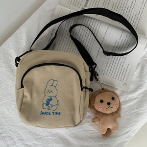 Detail of canvas crossbody bag with rabbit print, snack time text and lion plush charm