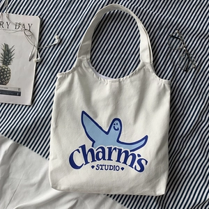 Detailed shot of white canvas tote bag with blue bird graphic and studio branding