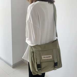 Detailed view of an olive green nylon messenger bag featuring buckled straps and brand label