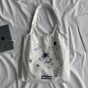 Detailed view of cream canvas tote bag with blue astronaut pattern and daily tech items