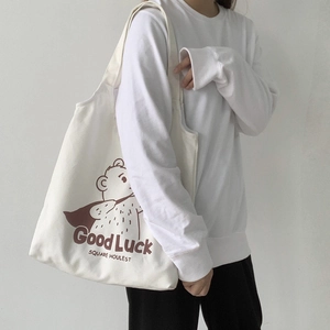 Detailed view of white canvas tote bag with brown cartoon bear and Good Luck lettering