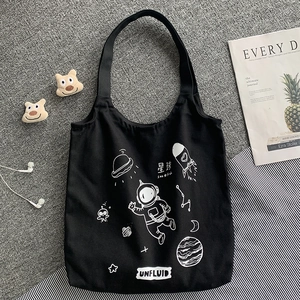 Flat lay of black canvas tote bag with white astronaut graphics and lifestyle props