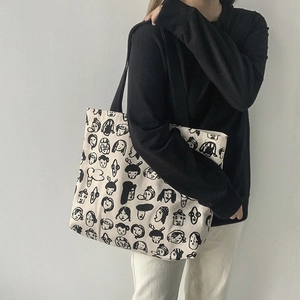 Detail of high-capacity canvas tote bag with artistic face graffiti and black shoulder strap