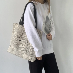 Detail view of canvas tote bag featuring vintage newspaper print and black wide handle straps