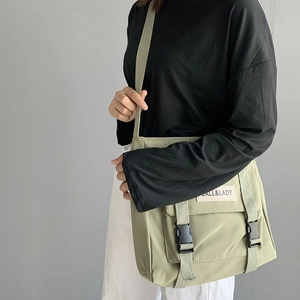Sage green nylon messenger bag with buckle closure worn as a crossbody by a model