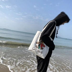 Détail du sac cabas blanc en toile avec motif ours coloré et texte GAME sur la plage