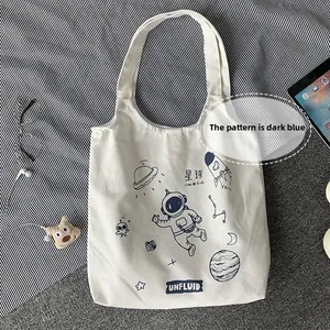 Detail of white canvas tote bag with dark blue space theme prints and wide handles