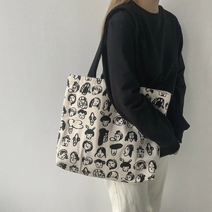 Close-up of minimalist canvas tote bag with black cartoon face illustrations and wide straps