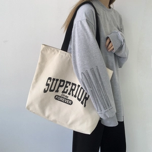 Detail of a large canvas shoulder bag with black straps and vintage text print on model