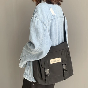 Model wearing a large black nylon messenger bag with buckle straps and logo patch