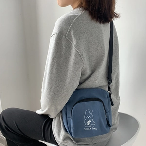 Detail of blue canvas crossbody bag showing cartoon rabbit print and snack time text