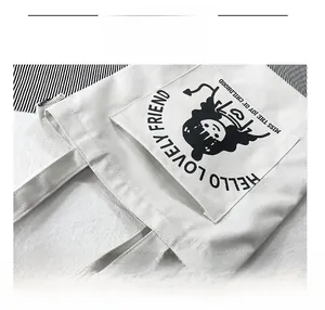 Detail of white canvas tote bag featuring front pocket and black cartoon character print