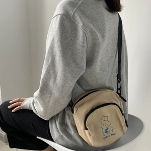 Close-up of beige canvas crossbody bag with cartoon rabbit print and black strap