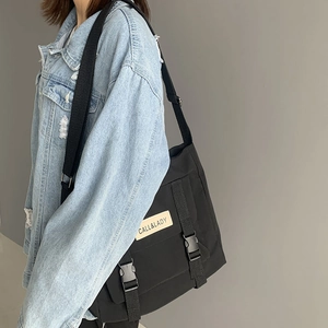 Detail of black nylon messenger bag with buckle closure and adjustable strap on a model
