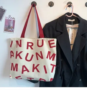 Detail of off-white canvas tote bag featuring bold red lettering and matching red handles