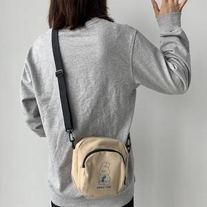 Cute beige canvas crossbody bag with cartoon rabbit design and adjustable black strap